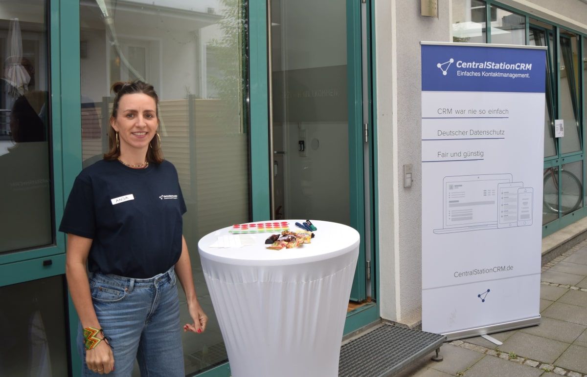 Anja steht neben einem Tisch und einem CentralStationCRM Banner am Eingang zum CRM Connect.