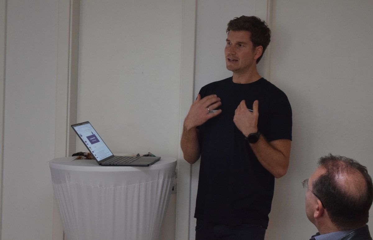 Axel erklärt CentralStationCRM auf dem CRM Connect. Dazu steht er neben einem Tisch, auf dem sich ein Laptop befindet und spricht zu Zuhörern außerhalb des Bildes, sowie zu Michael, der aufmerksam zuhört.
