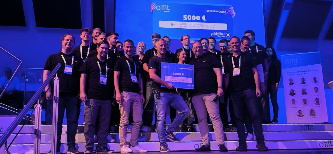 Das Team von Goldsilbershop zusammen mit Mario Jung auf der OMT Bühne. Ein 5.000 Euro Scheck, der gespendet wird.