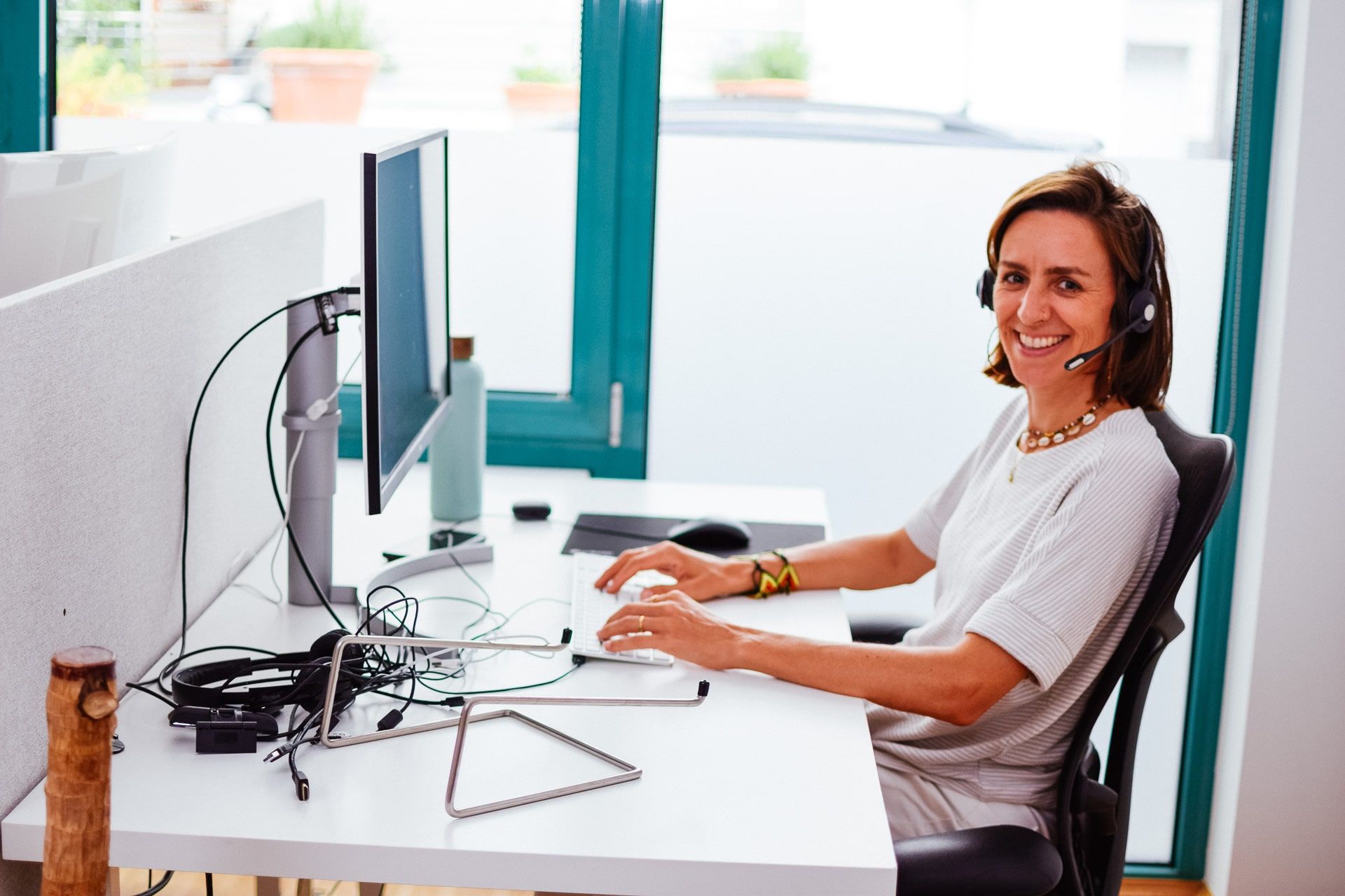 Anja sitzt am Computer mit Headset und lächelt in die Kamera.